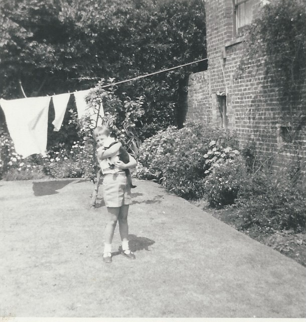 The back garden of an old cottage with washing drying on a line and a young child holding a black and white cat