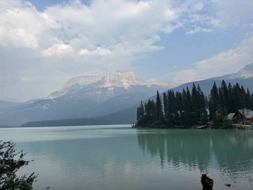 photo of the Emerald Lake, British Columbia, looking more pale greenish blue with pine forest and a mountain in the background beneath a partly cloudy sky